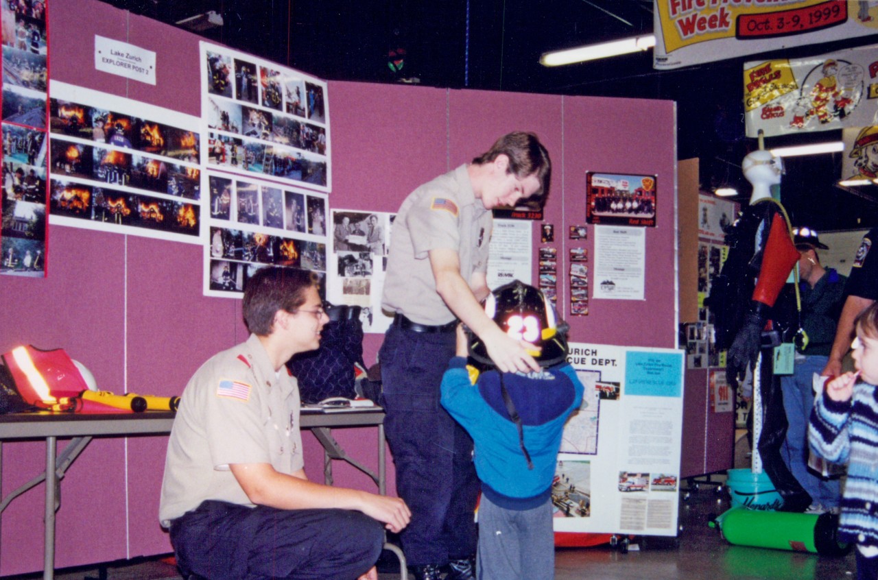 During fire prevention week, the local Boy Scout troop volunteer assisting kids with trying on equipment