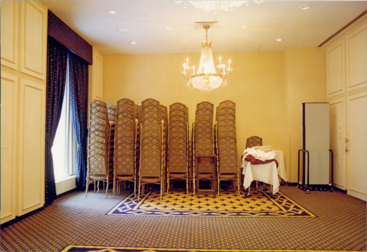 A closed portable room next to several stacks of chairs