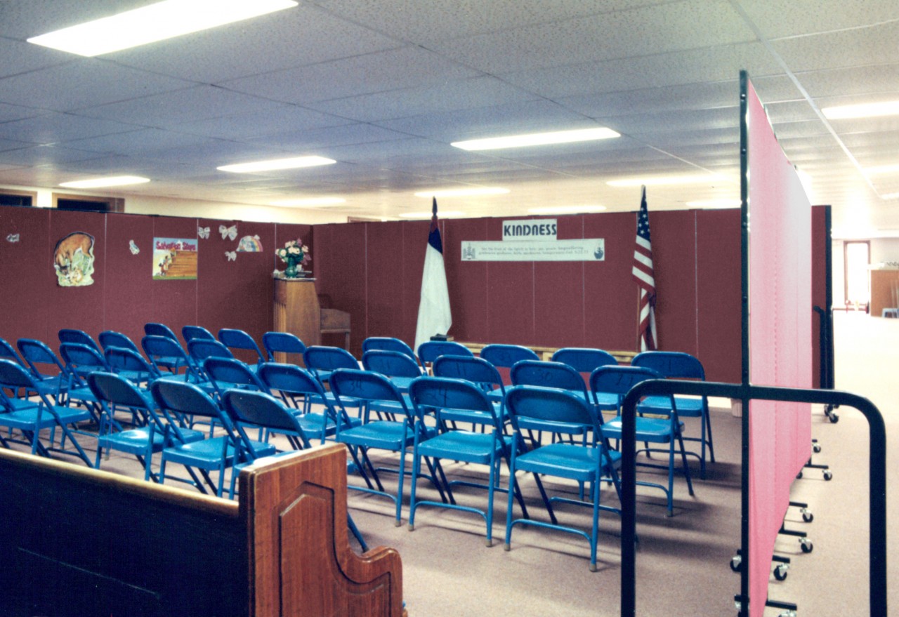 4 rows of blue foldable chairs are surrounded by red room dividers