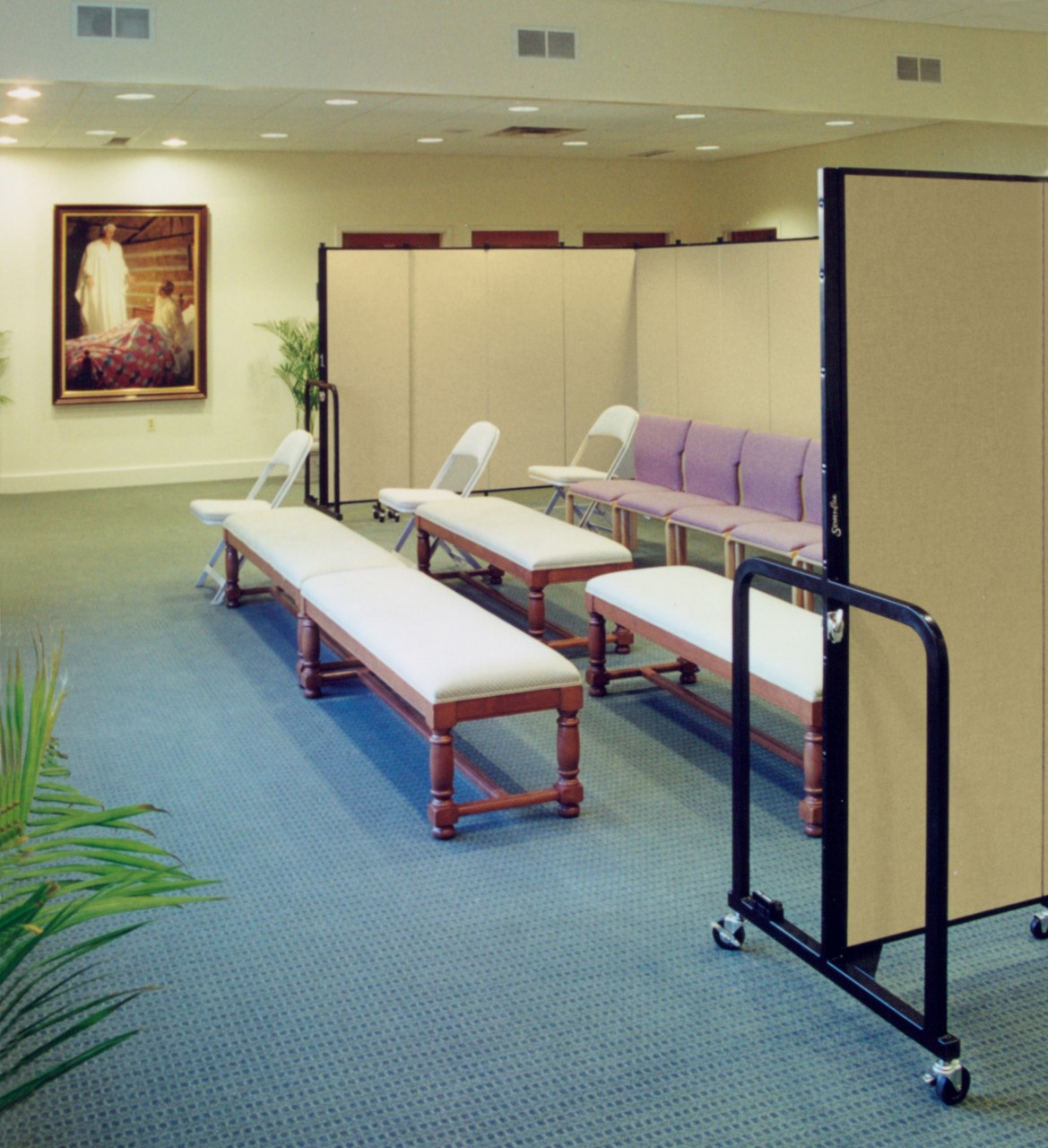 A row of chairs follows two rows of benches in a prayer room that are shielded by a set of room dividers