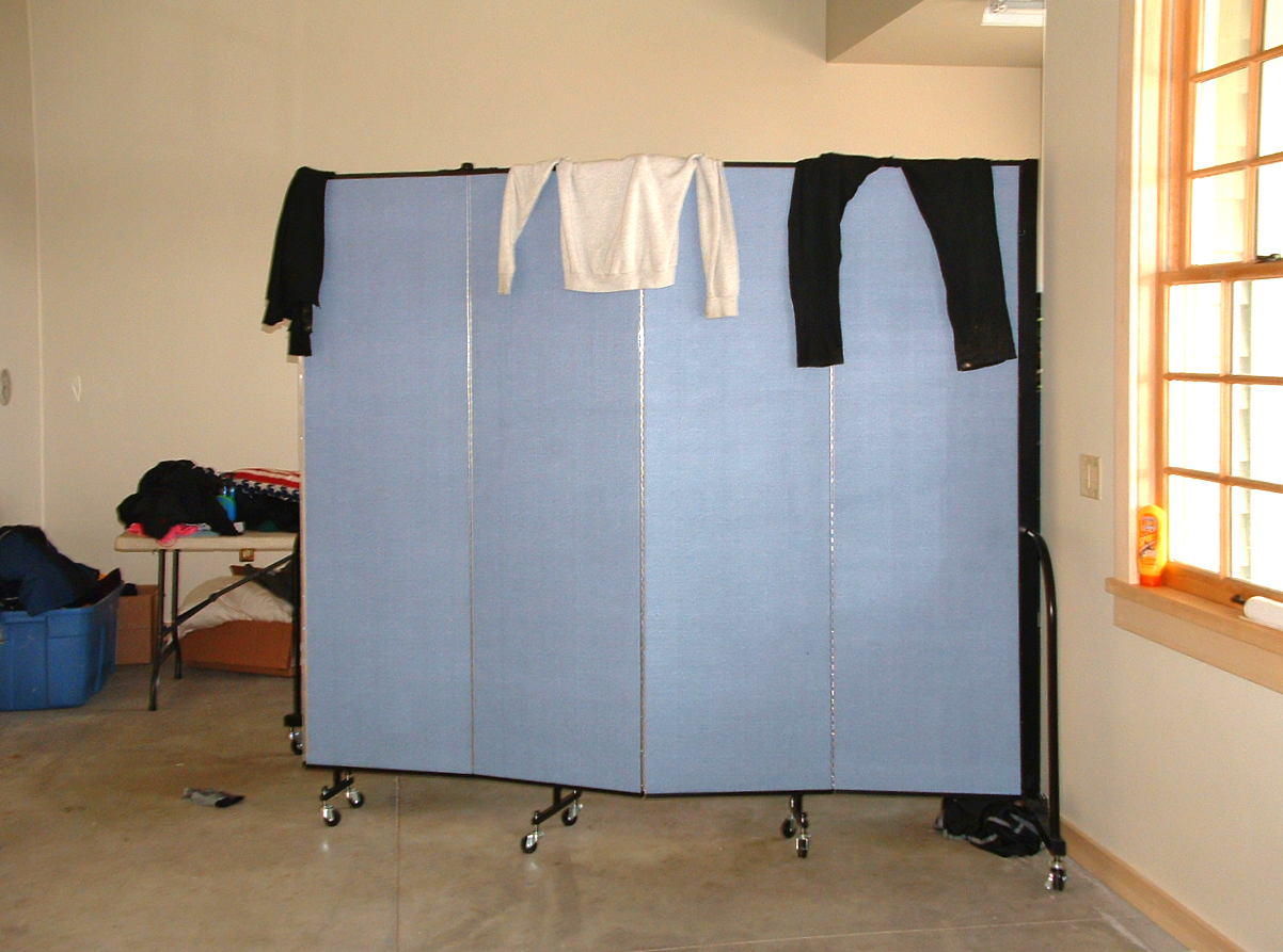A table of clothes is stored behind a room divider in the corner of a room where clothes are draped over the top of the divider