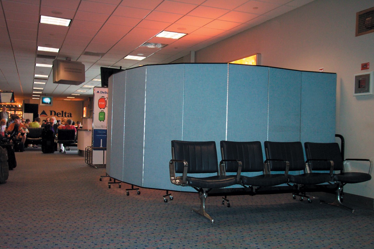A blue room divider arranged in a half circle hides a screening area in an airport
