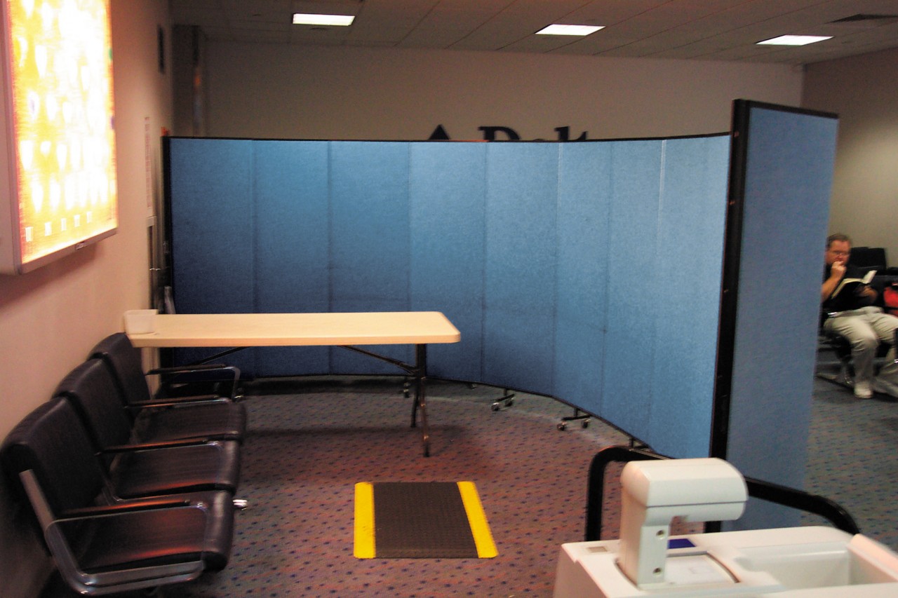 A blue room divider on wheels separates a medical waiting area and a screening room