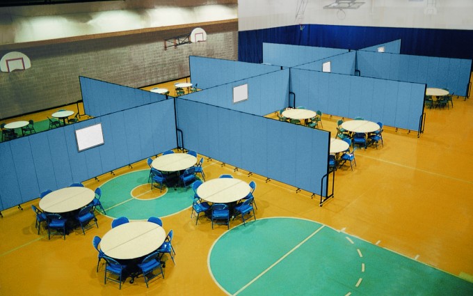 Blue room dividers are used to create eight classrooms in a school gymnasium Several blue room dividers are used to divide round tables and chairs in each of the eight classrooms