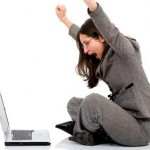 A business woman sits on the floor looking at a computer celebrates with her arms up A woman sits on the floor looking at a computer celebrates with her arms up