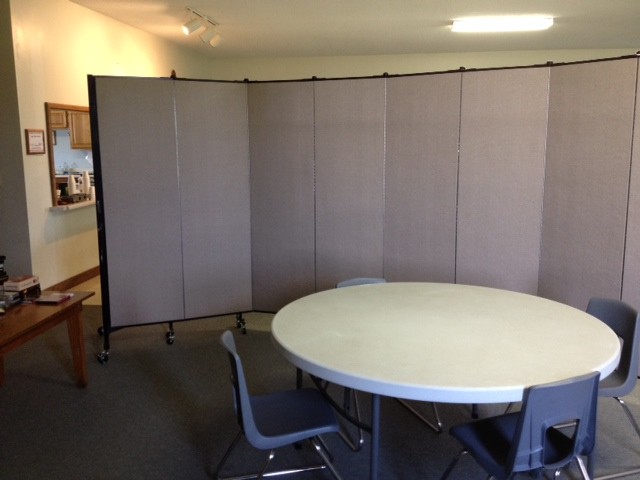 A Screenflex Room Divider divides a round table and chairs from a church dining room