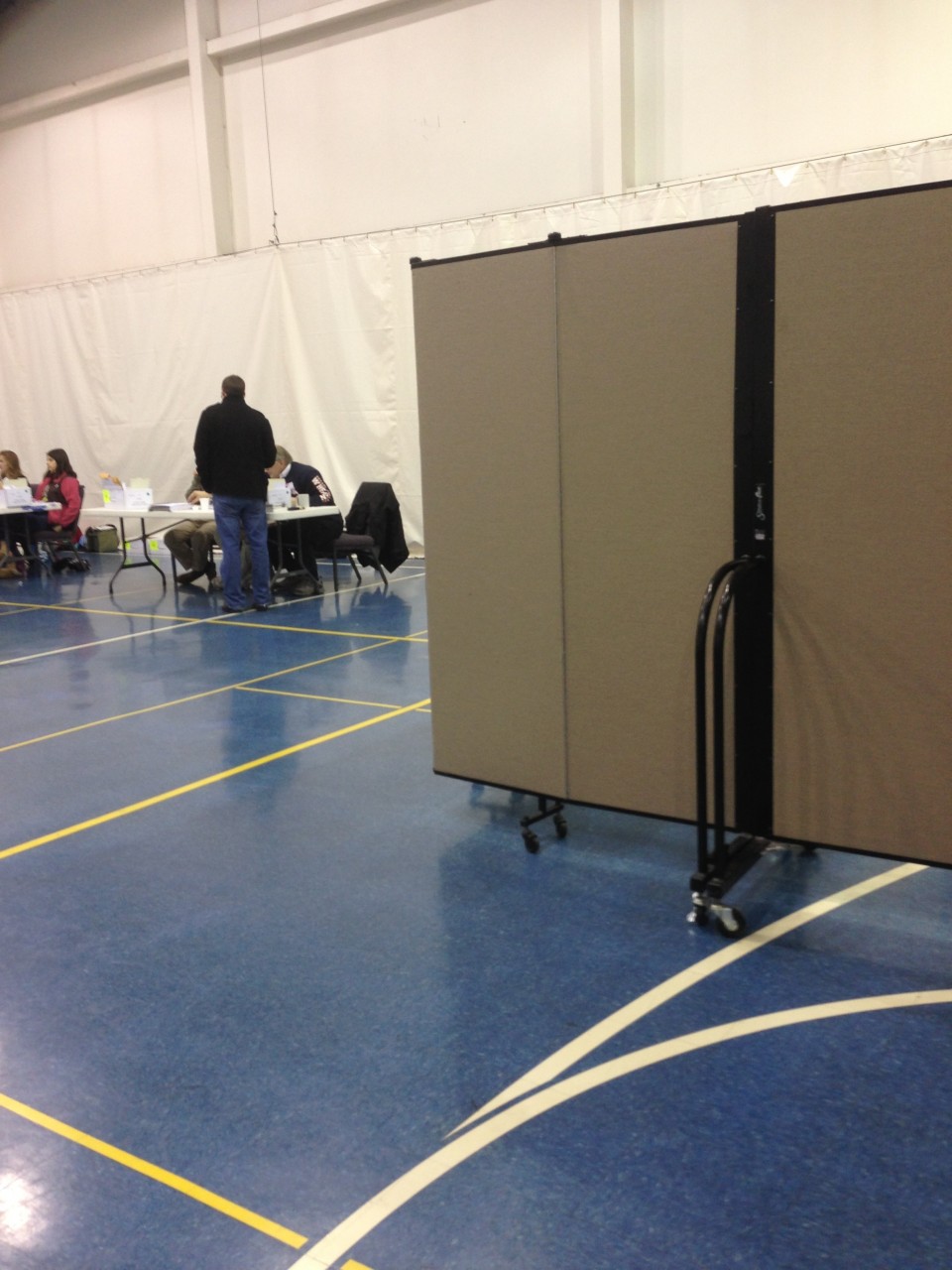 Man speakes to election judge at a table in a gym