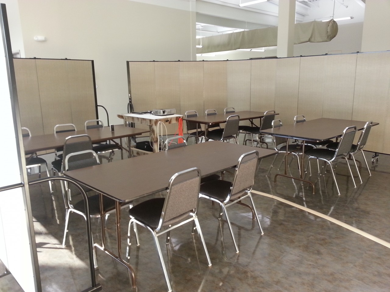 4 rectangular tables and chairs surround a projector in a temporary meeting room created with Screenflex Room Divider walls.