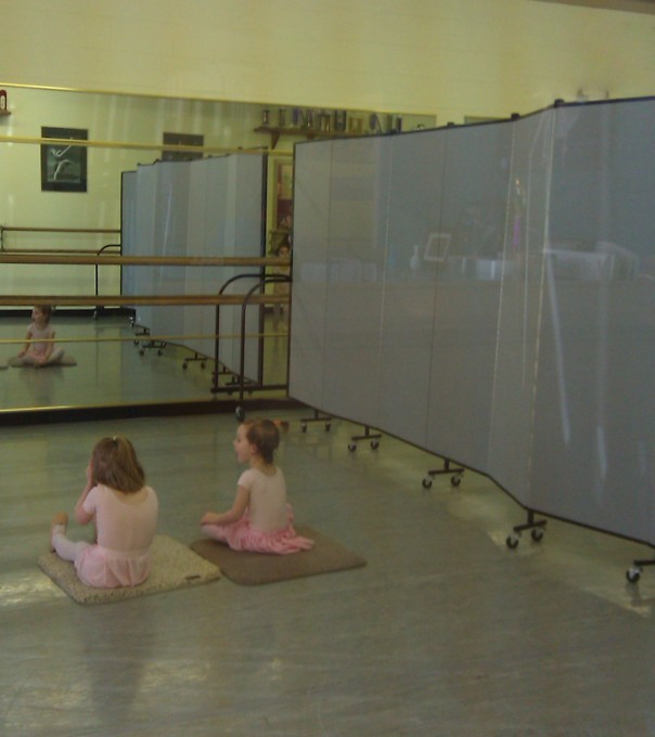 Two young dancers in pink leotards sitting on a mat in a dance studio