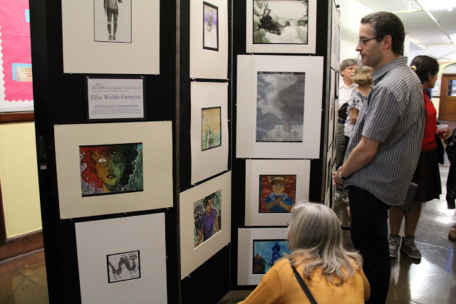 Gallery goers look at art displayed on display panels in a hallway.