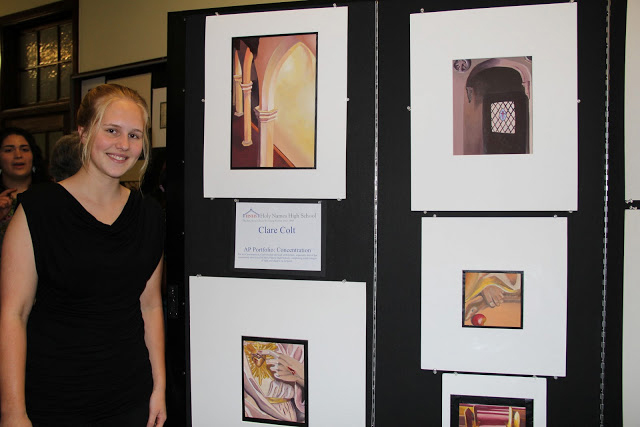 Female art student stands beside her drawing on display at an art gallery