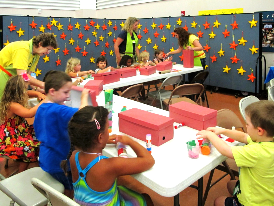 Red and Yellow stars hang from a Screenflex Divider behind students that are sitting at tables decorating shoe boxes.
