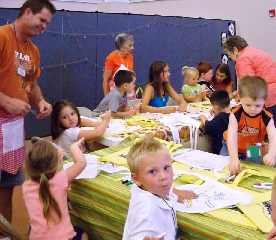 Male and Female adults helps young students Colors pictures during craft time at a VBS camp.