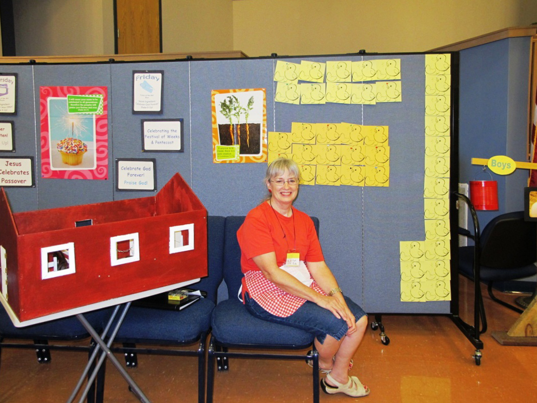 A lady sits on a chair next to a game board created on a portable room divider.