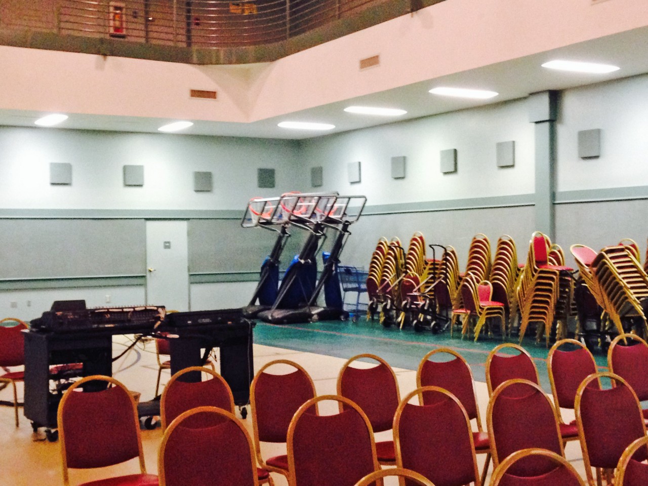 Rows of chair are set up to create a church sanctuary inside a gym. Additional chairs and basketball hoops are set out of the way against the wall.