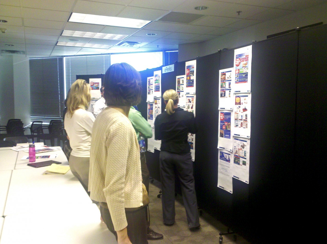 A small group of employees review several storyboard layouts tacked to a black Screenflex Room Divider.