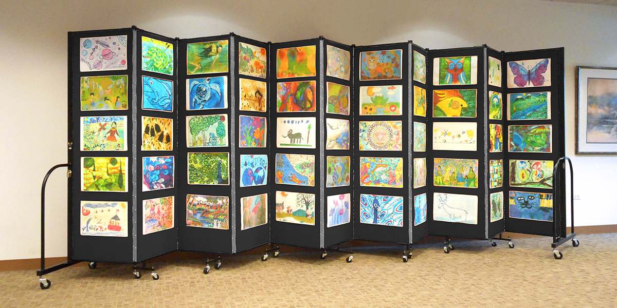 Colorful children artwork tacked to folding partiton walls A black accordion room divider decorated with Colorsful children artwork