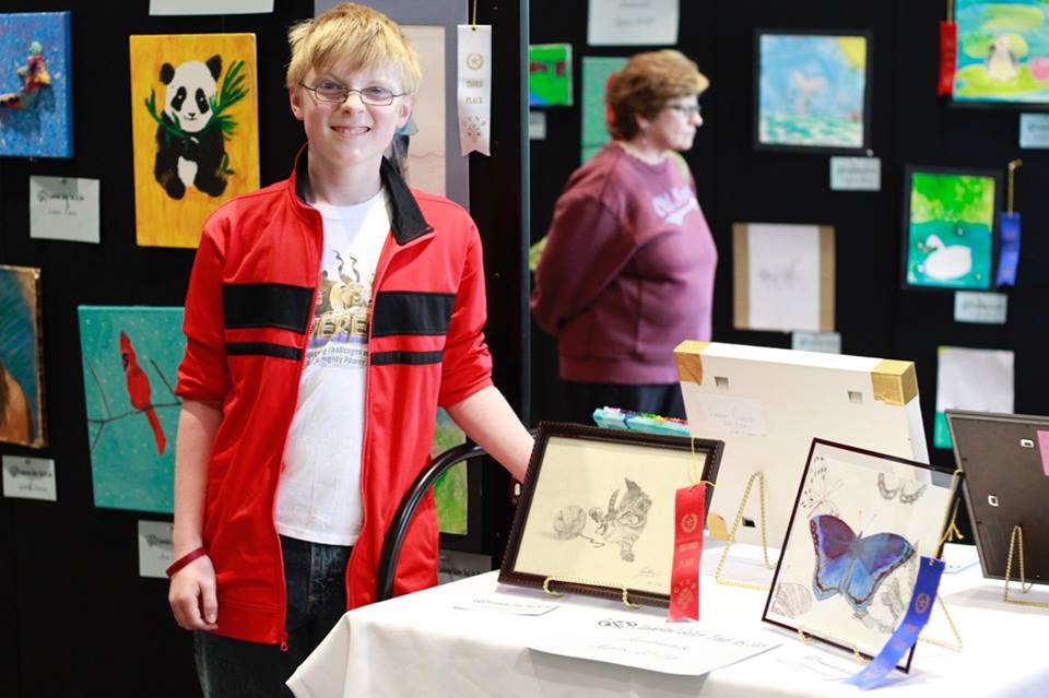 An teen art show contestant poses with his artwork on a table