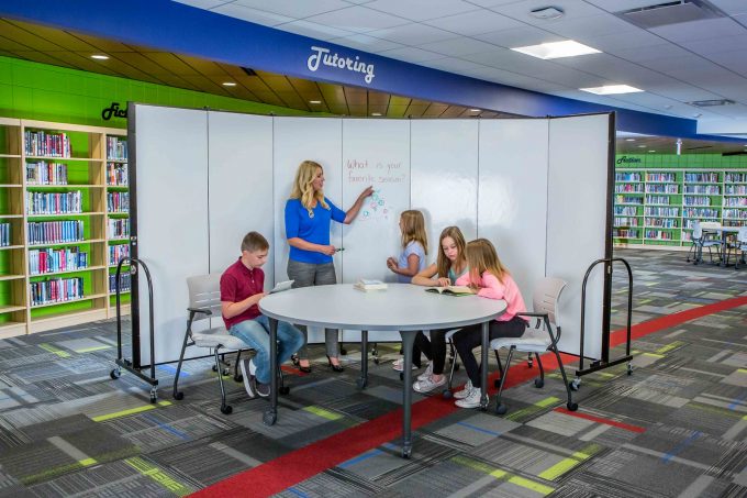 A teacher and students in a tutor room writing on whiteboard walls 