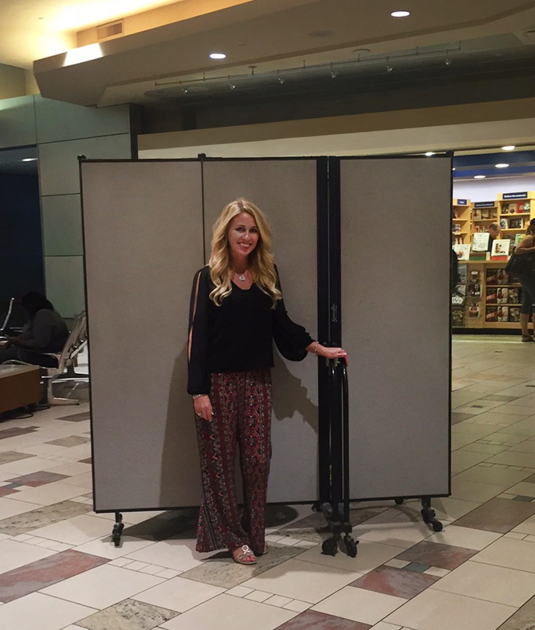 A woman stands in front of a portable wall on wheels in an airport