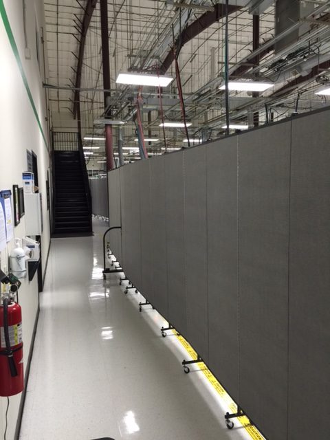 A long line of portable room dividers separate a portion of a factory from other employees