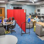 A set of students on each side of a portable room divider splitting a classroom in two